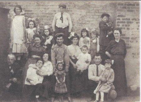 My grandparents in 1912 with Grandpa kneeling with Nettie on his knee and Willy on Grandma's lap, Mary standing behind baby Willy and Sarah at top left with long white dress along with aunts, uncles and cousins ... plus dog, girl with flag, and old man chewing tobacco. 